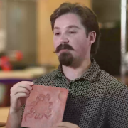 Christopher Gaines holds clay-colored square with a tactile representation of a sun petroglyph