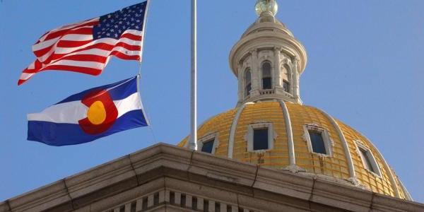 A view of the U.S. and Colorado state flags flying over the Colorado State Capitol Building.